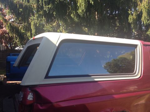 1993 Ford Bronco - A red SUV with a white camper shell is parked next to a blue truck.