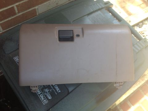 1993 Ford Bronco - A tan glove box door is shown, detached from a vehicle, resting on a textured surface.
