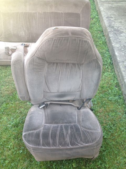 1993 Ford Bronco - A worn taupe fabric car seat, likely from a parts vehicle, is shown outdoors.