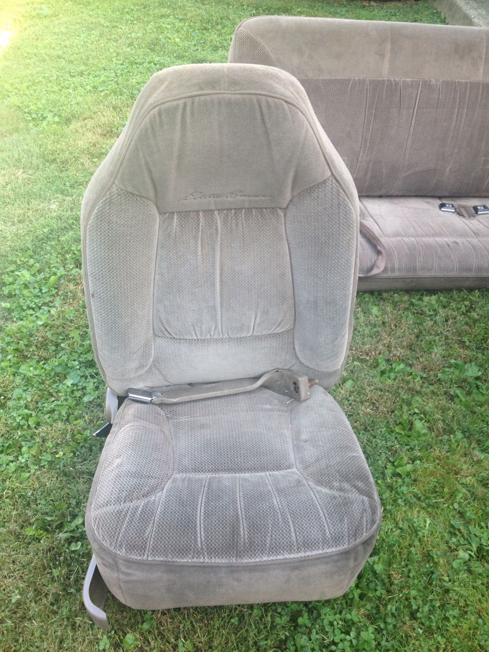 Front car seat and rear bench seat on grass. Seat fabric is grey with vertical stitching