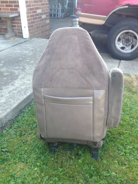 1993 Ford Bronco - A tan car seat is shown from the back, with a pocket on the rear. A portion of a red vehicle is visible in the background.