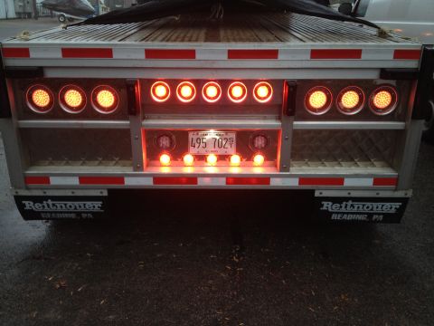 2003 Peterbilt 379 - The rear of a trailer is illuminated by numerous lights, a license plate and manufacturer branding on the mudflaps.