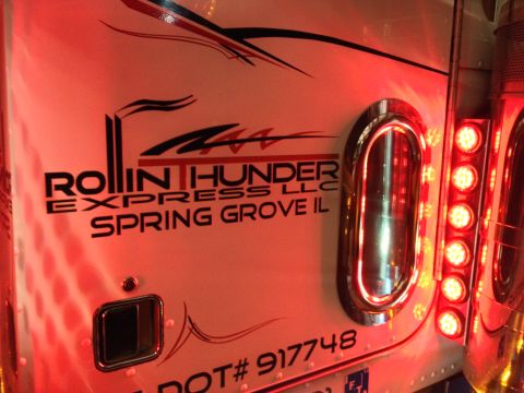 2003 Peterbilt 379 - Close-up of a truck's side panel, displaying company decals and illuminated red lights.