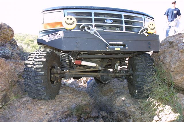 Ford Bronco with big tires on rocks, has a winch and two yellow lights with smiley faces