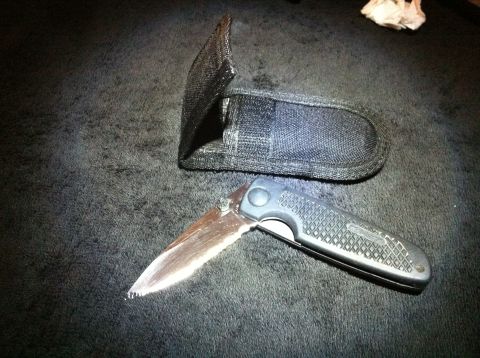 1984 BMW 3 Series - A folding knife and its sheath are displayed on a dark, textured surface.