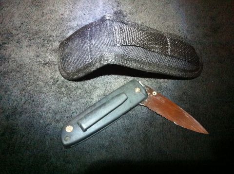 1984 BMW 3 Series - A folding knife and its sheath are shown against a dark, textured background.