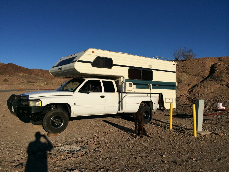 White pickup truck with camper shell parked in a desert landscape