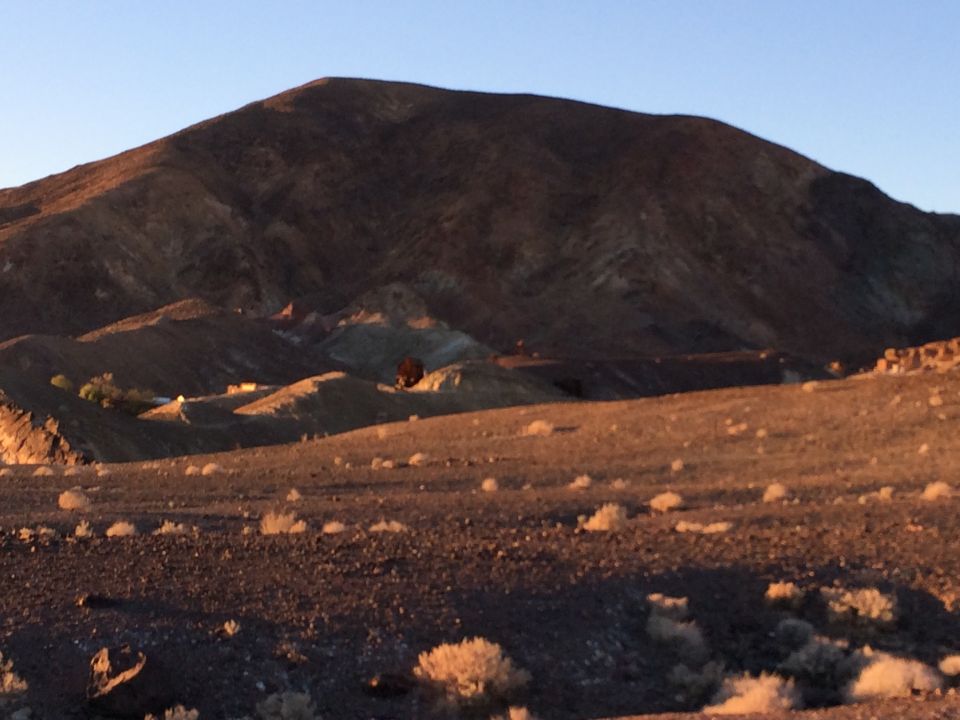 desert hills at sunset with a few scattered buildings and a dark object that might be a vehicle in the distance