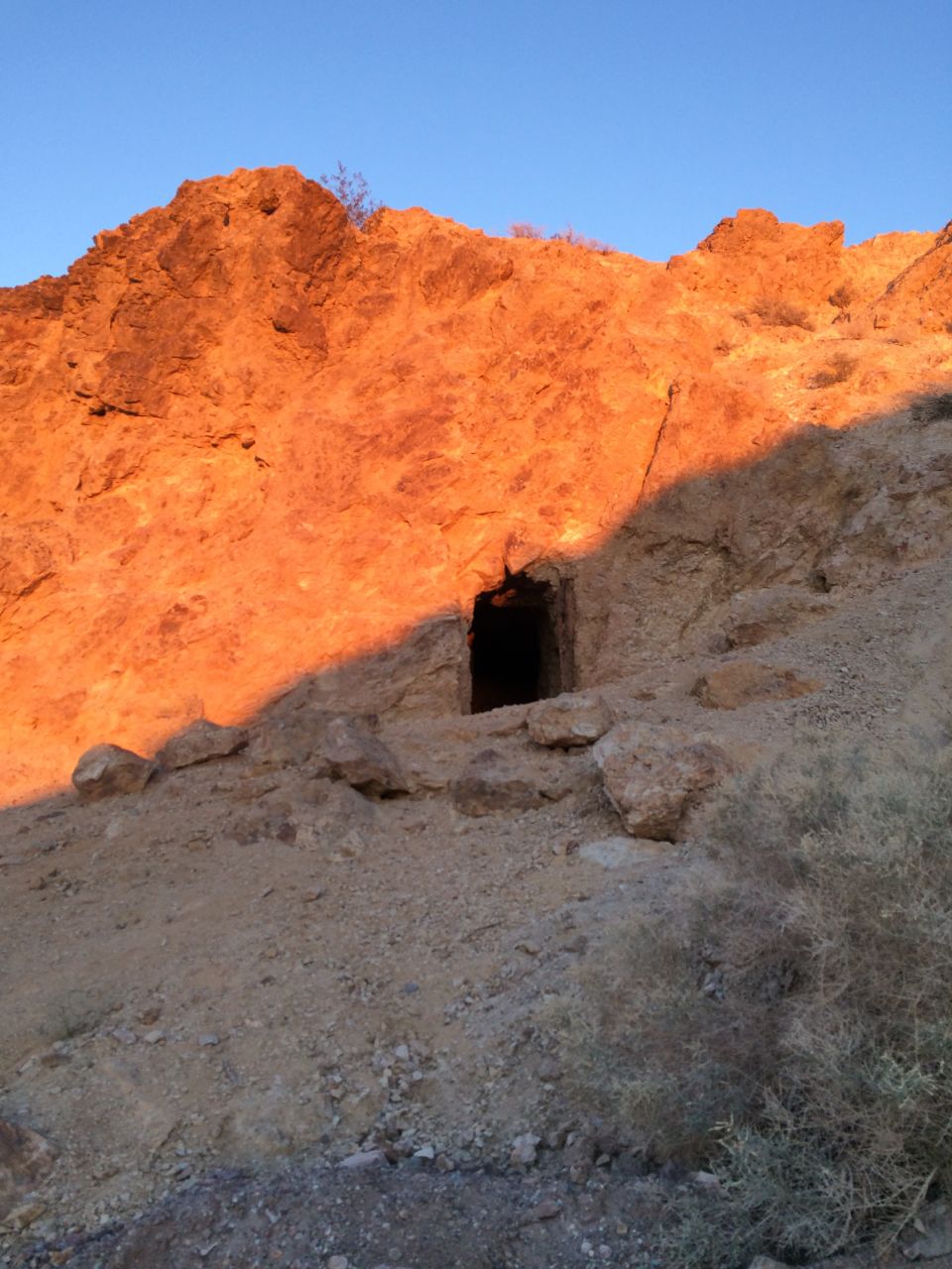 Cave entrance in a rocky hillside at sunset