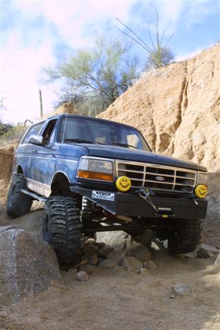 1994 Ford Bronco - This modified Ford Bronco is shown off-roading on a sunny day with a clear blue sky.