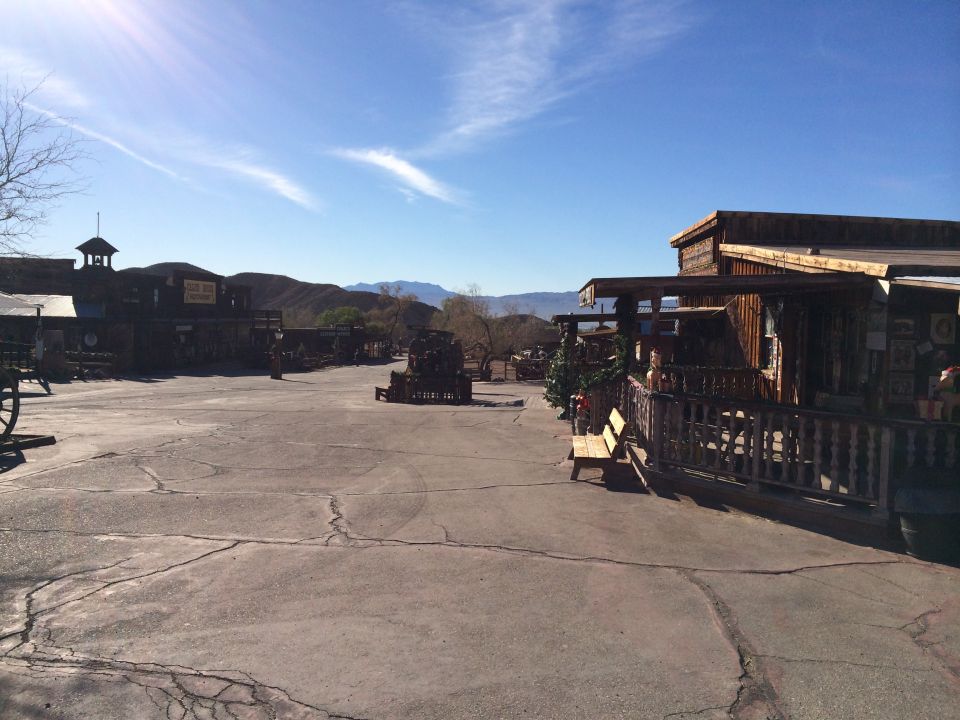 Desert town with wooden buildings and a paved lot under a blue sky