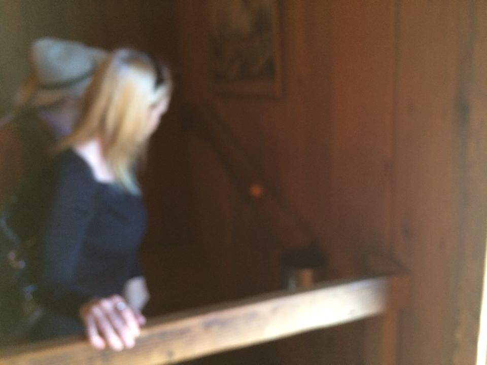 Two people inside a rustic wooden structure, one with blonde hair and a black top, leaning on a railing