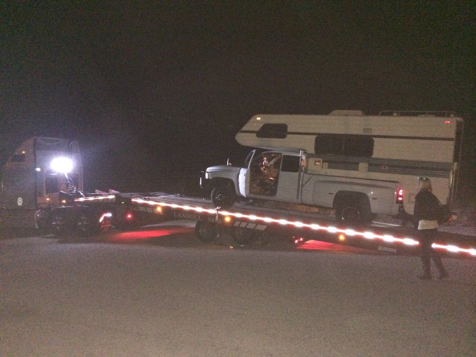 White pickup truck with camper on a flatbed trailer at night