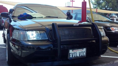 2003 Ford Crown Victoria - black Ford Crown Victoria with a push bar and 'EVIL VIC' plate parked under a gas-station canopy.