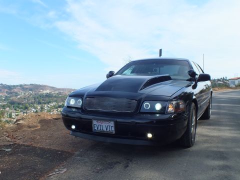 2003 Ford Crown Victoria - black Ford Crown Victoria with halo headlights and an 'EVIL VIC' plate parked on a hilltop overlooking a valley.