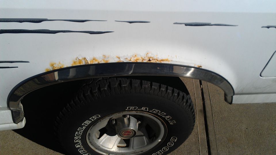 Rust along white fender arch above chrome trim, Goodyear Wrangler tire on alloy wheel