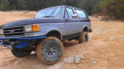 1990 Ford Bronco - A modified Ford Bronco navigates a challenging off-road terrain with its tires deep in the mud.
