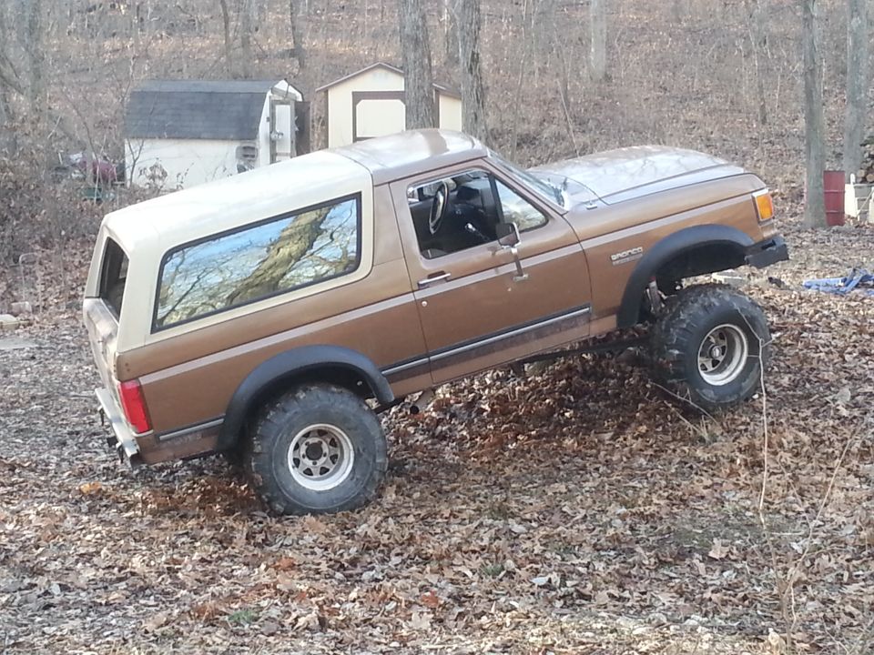 Brown 1987 Ford Bronco with lifted suspension and off-road tires on a dirt hill
