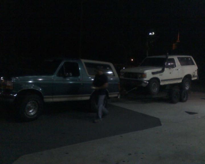 Green 1996 Ford Bronco towing a white Ford Bronco at night