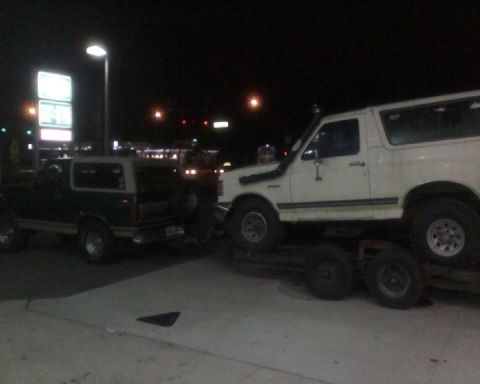 1996 Ford Bronco - Two Ford Broncos are visible at night, with one loaded onto a trailer.