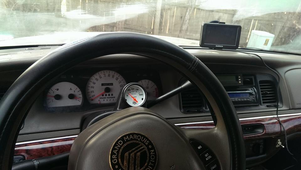 Interior shot of a 2000 Mercury Grand Marquis showing the steering wheel, dashboard gauges, and a Garmin GPS unit