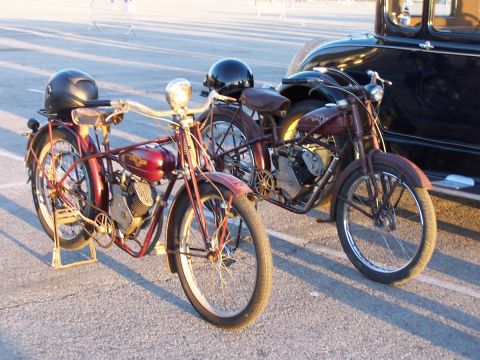 1990 Ford Bronco - Two vintage motorcycles are parked next to a classic black car, with helmets on the front bike.