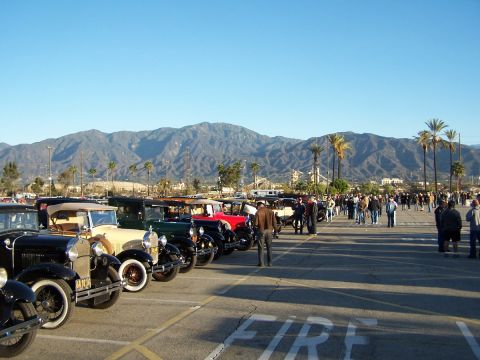 1990 Ford Bronco - A collection of classic automobiles are lined up in a parking lot, with a scenic mountain range visible in the distance under a clear blue…