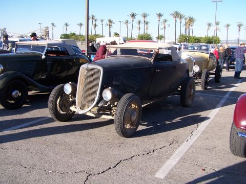 1990 Ford Bronco - A black 1933 Ford hot rod convertible is parked in a lot with other classic cars.