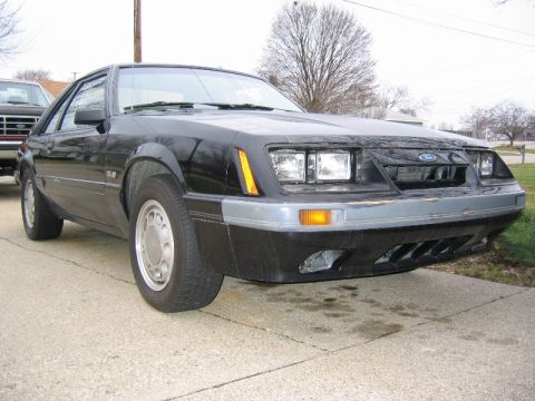 1985 Ford Mustang - A black 1985 Ford Mustang GT is parked on a driveway, with another vehicle visible in the background.