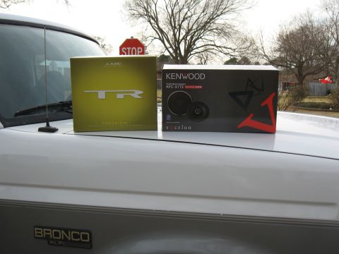 1994 Ford Bronco - Two car audio speaker boxes sit on the hood of a white 1994 Ford Bronco, with a stop sign visible in the background.
