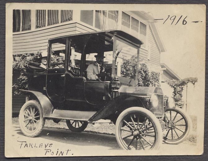 1916 Ford Model T Touring Car with two passengers, parked in front of a house