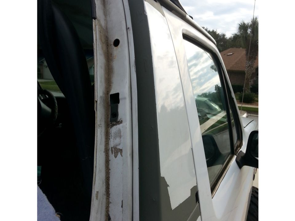 Close-up of a white vehicle's door frame with peeling paint and rust stains. Interior visible through the window