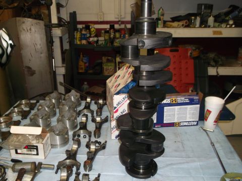 1967 Ford Mustang - Engine parts, including a crankshaft and several pistons, are displayed on a workbench in a garage setting.