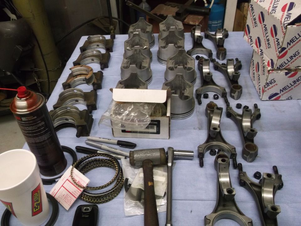 Engine parts including pistons, connecting rods, and bearings laid out on a table with Melling boxes