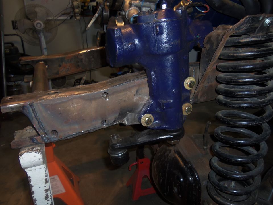 Blue painted steering gearbox mounted to a metal bracket, with a large coil spring and suspension components visible
