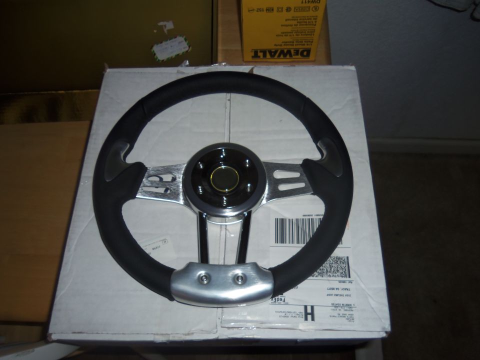 Aftermarket steering wheel with black grip and chrome spokes, resting on a cardboard box