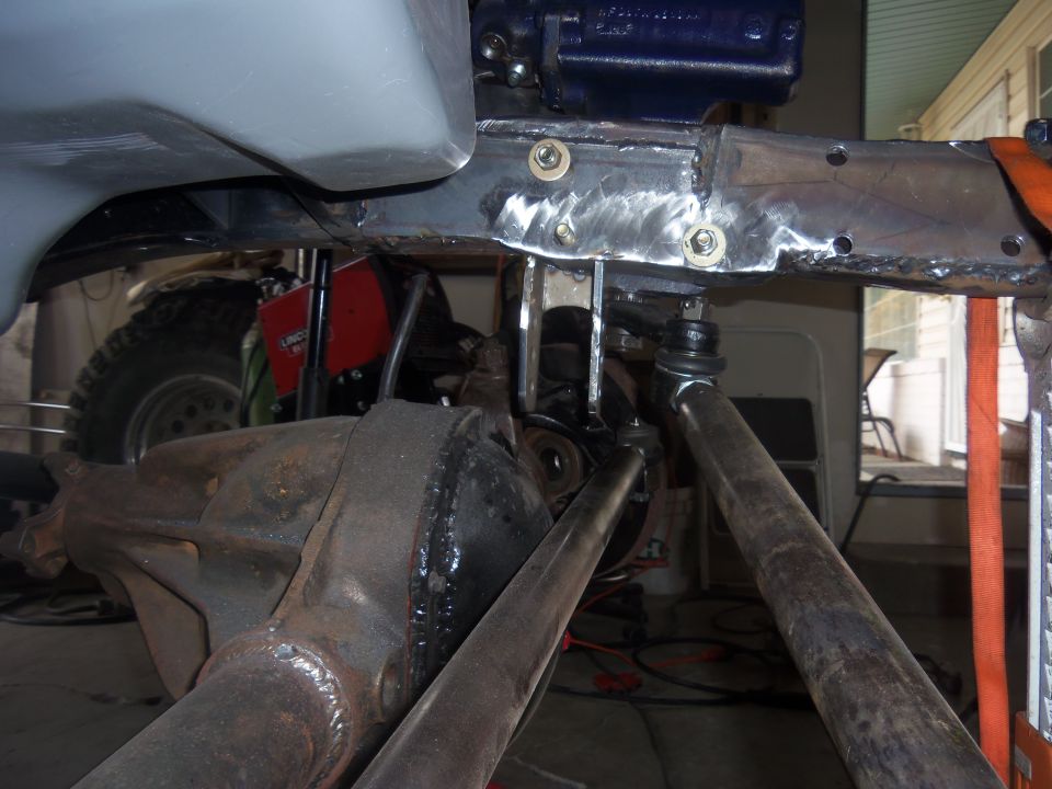 close-up of vehicle frame with suspension parts and a large tire visible in background