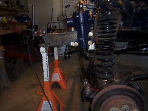 1968 Ford Bronco - Close-up of vehicle suspension and steering components, including a coil spring and steering box, supported by jack stands.