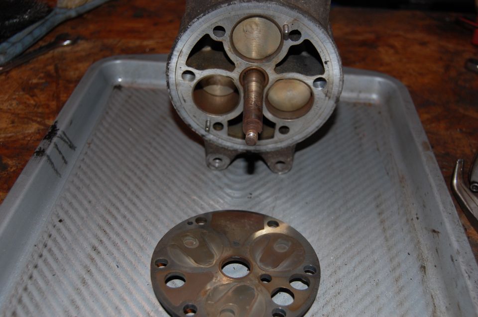 Disassembled pump housing with three pistons and a round valve plate laid on an aluminum tray on a workbench