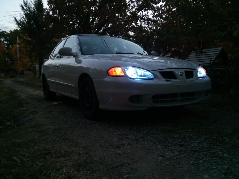 White Hyundai Elantra with aftermarket headlights parked on a gravel driveway