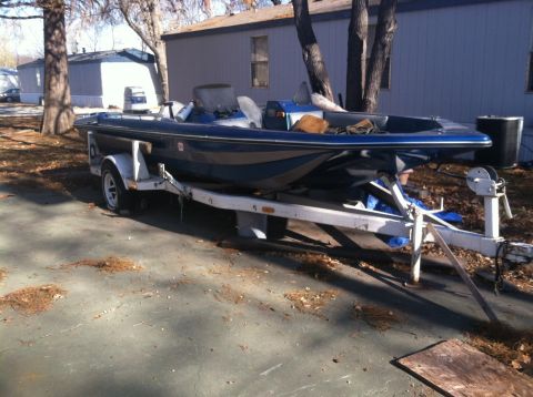1986 Ford Bronco - A blue and gray boat is parked on a trailer in a driveway next to some mobile homes.