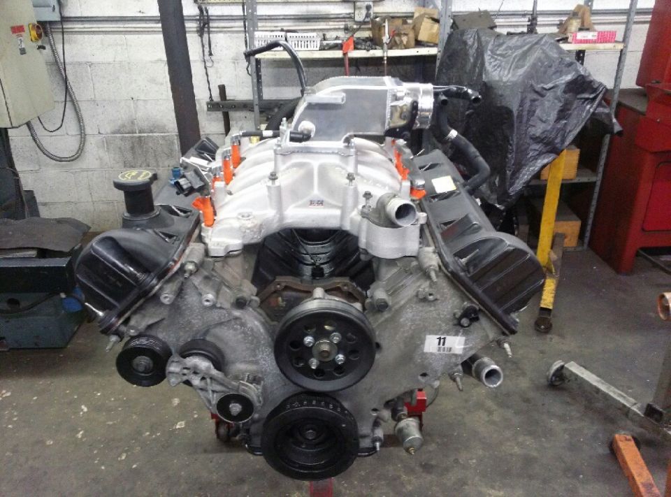 Aluminum-intake V8 engine assembly on a stand in a workshop, viewed from the front pulleys