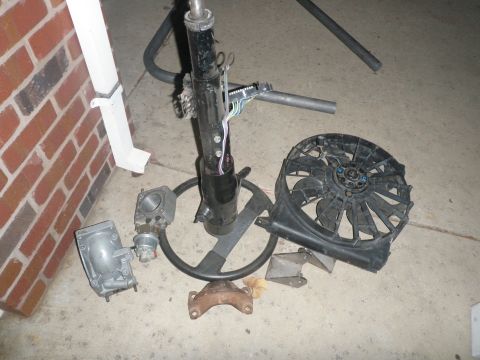 1961 International Scout 800 - Various vehicle parts including a steering column, fan, carburetor, and engine mount are laid out on a concrete surface.