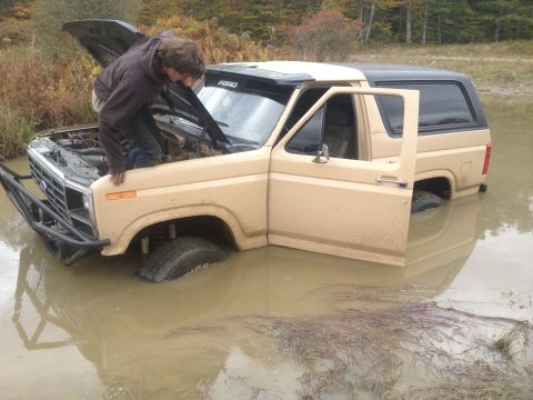 1970 Ford F-250 - A person checks the engine of a Ford Bronco submerged in water.