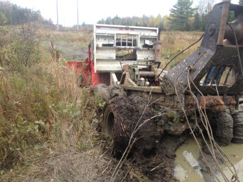1970 Ford F-250 - A tow truck and its trailer are deeply stuck in mud and vegetation, indicating a difficult recovery situation.