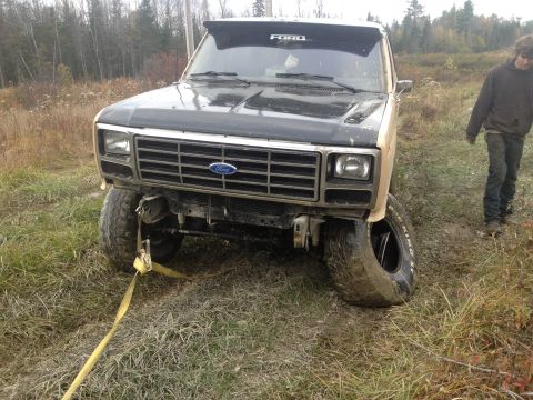 1970 Ford F-250 - Ford truck stuck in mud with a flat tire and a tow strap attached.