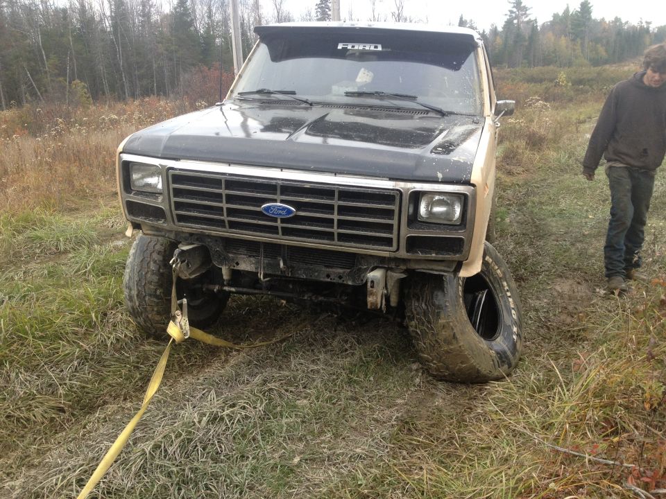 Ford truck with flat tire stuck in muddy field, tow strap attached to front bumper