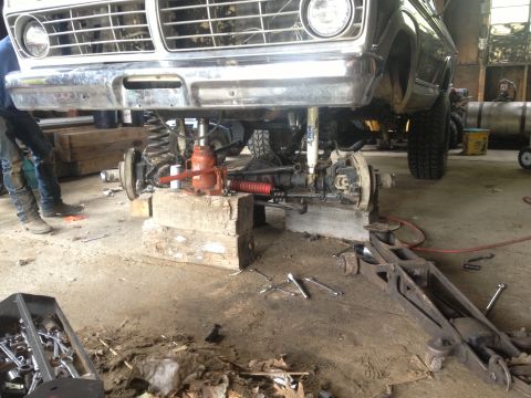 1970 Ford F-250 - Front axle and suspension of a 1970 Ford F-250 undergoing maintenance with a jack and blocks supporting the frame.