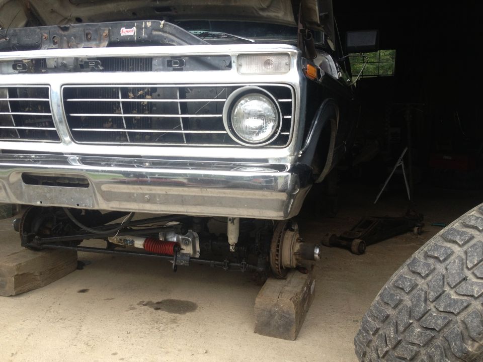 Black Ford truck front end with chrome grille and bumper, raised on blocks with front wheels removed