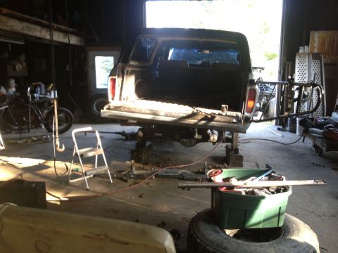 1970 Ford F-250 - A pickup truck is elevated in a garage, with its tailgate down and bed open, surrounded by tools and equipment.